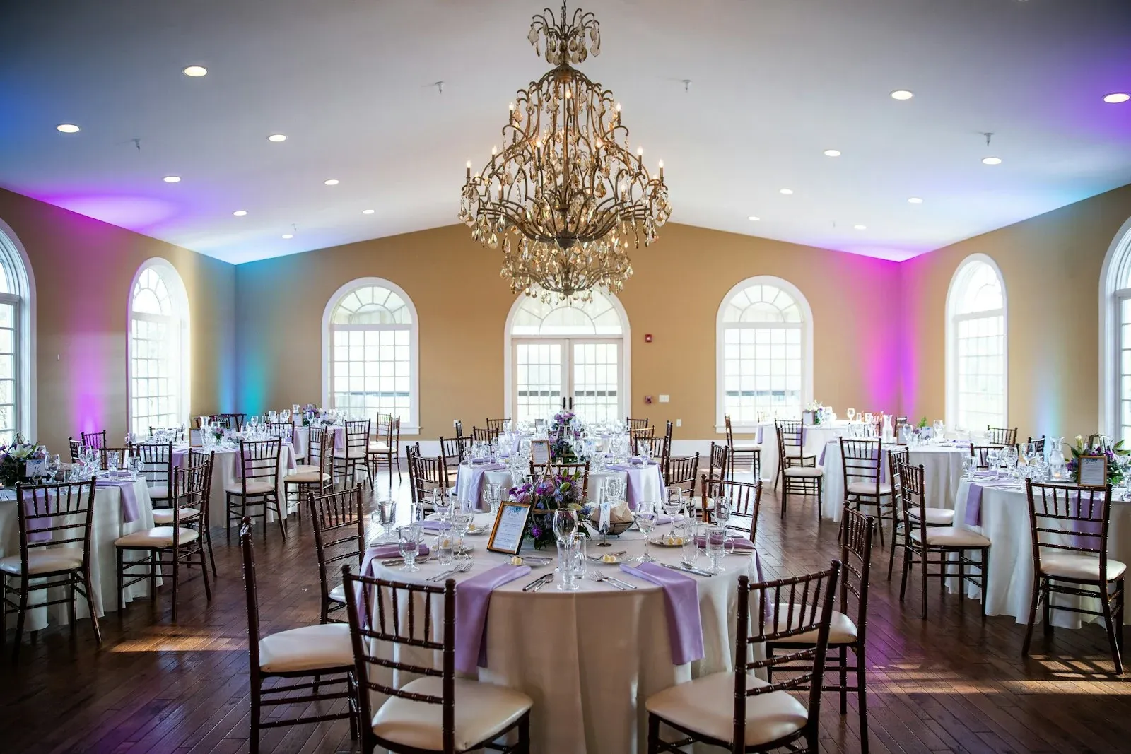 Formal celebration tables under chandeliers with purple and gold lighting